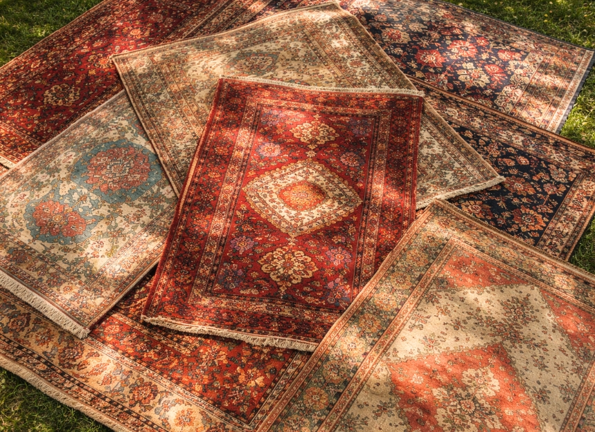 Vintage handmade rugs layered on grass with sunlight and shadows top view